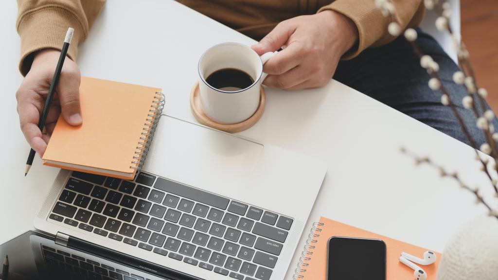 Person holding a coffee mug next to a laptop