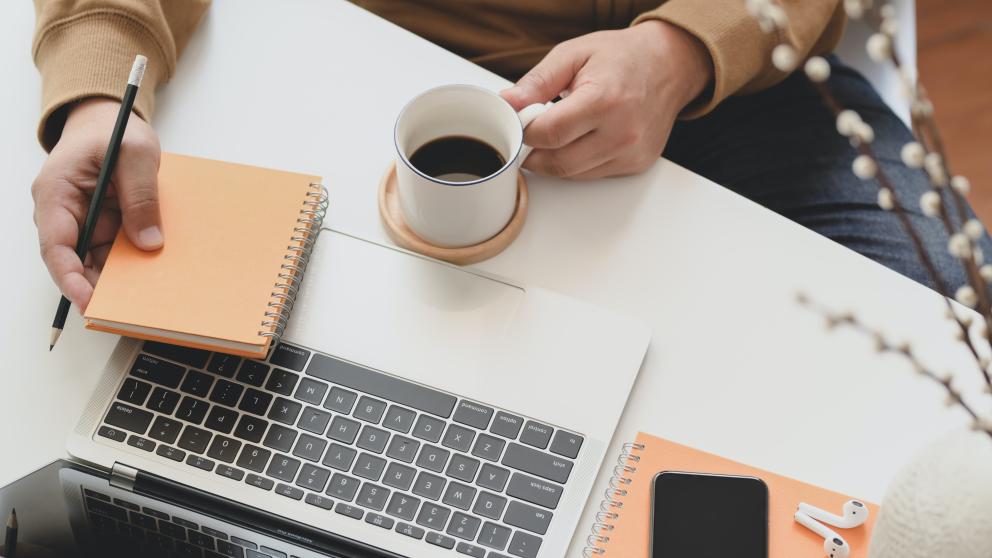 Person holding a coffee mug next to a laptop