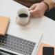 Person holding a coffee mug next to a laptop