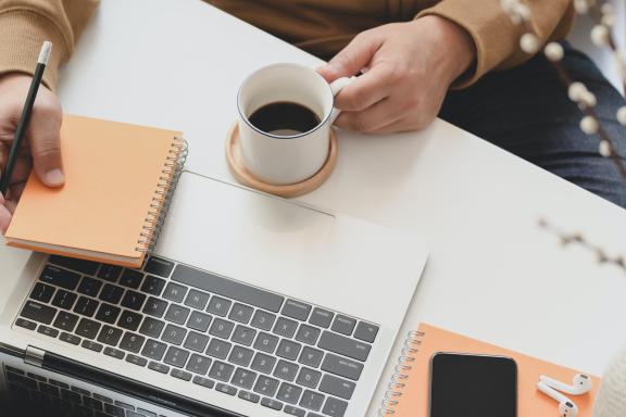 Person holding a coffee mug next to a laptop